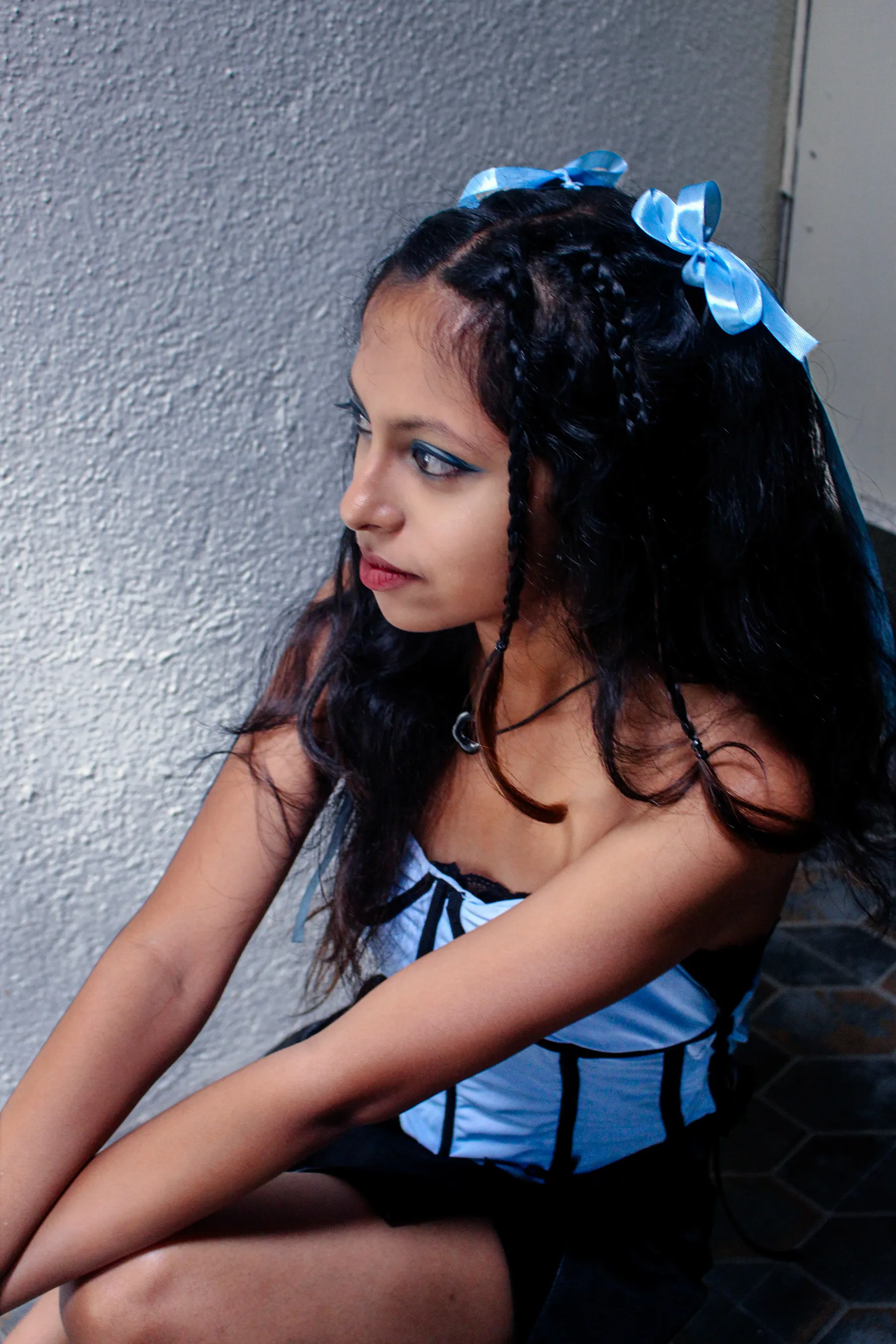 The model seated in the pale blue corset against a grey wall