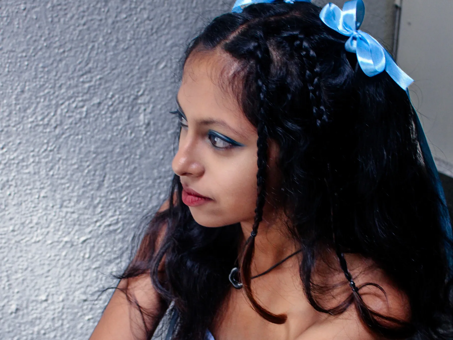 The model in profile against a grey wall, with braids and a blue ribbon