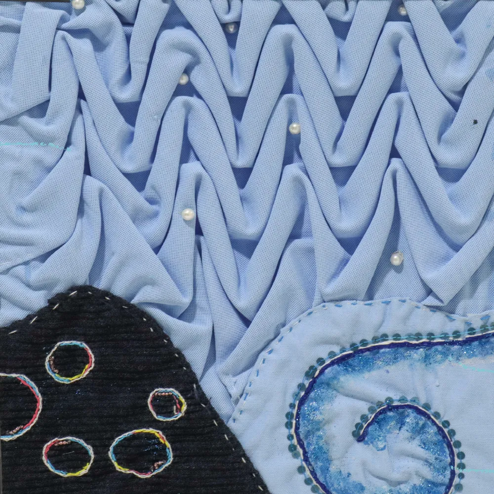 Close-up of sample 2: pale blue wave smocking with pearls, a black appliqué with embroidered bubbles, and a sequinned spiral