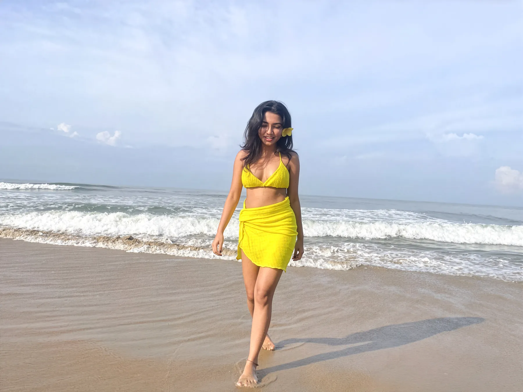 The model walking along the shoreline in a yellow two-piece and sarong