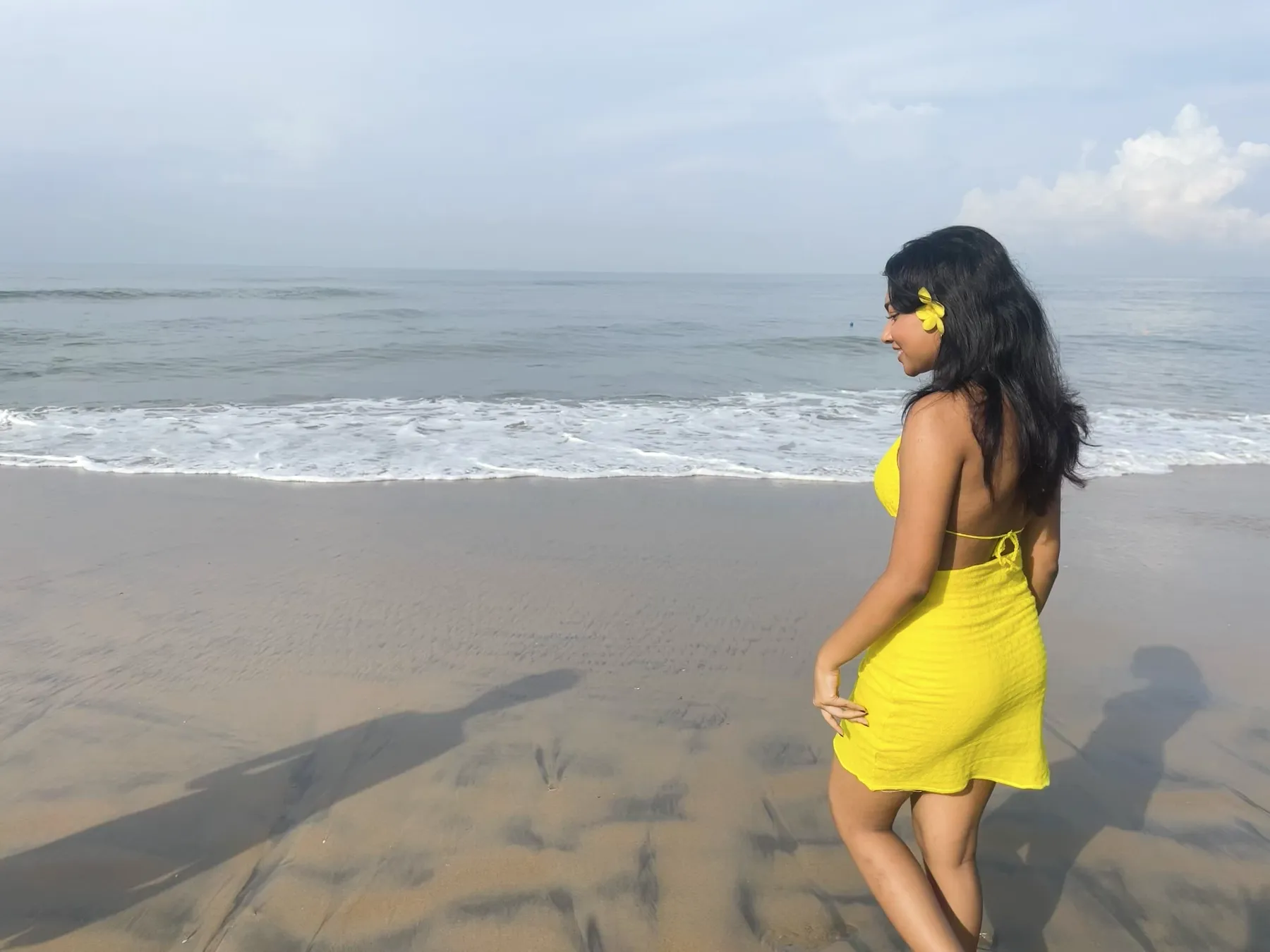 The model on the shore, seen from behind, with a yellow flower in her hair