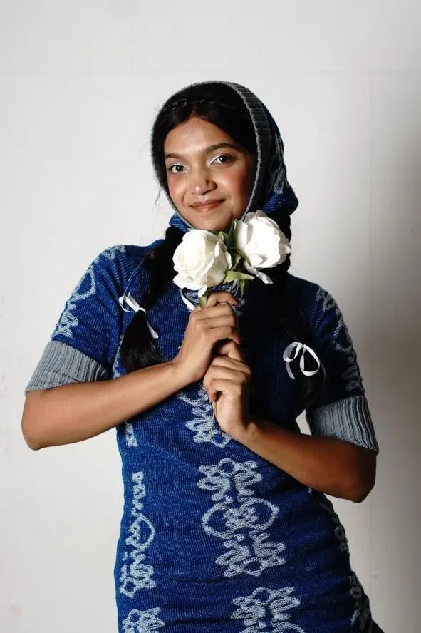 The model holding white flowers, wearing the blue knitted dress